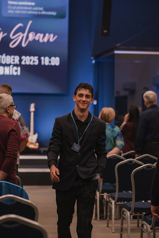 Mladý muž prichádza do sály, úsmev.